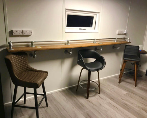 Industrial scaffold board pub bar with galvanized pipe clamps and a long wooden top with three stools.