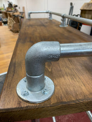 Industrial scaffold board pub or breakfast bar with galvanized pipe railing and elbow joint.