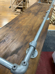 Industrial scaffold board pub or breakfast bar with galvanized pipe rails and clamps on dark wood surface.