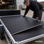 Person handling a large black sheet of material on a flatbed truck with SylkBuild branding.