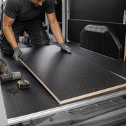 Person installing black rubber matting in a vehicle with tools on the floor.