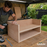 Man assembling a wooden shelf outdoors with tools and materials around.