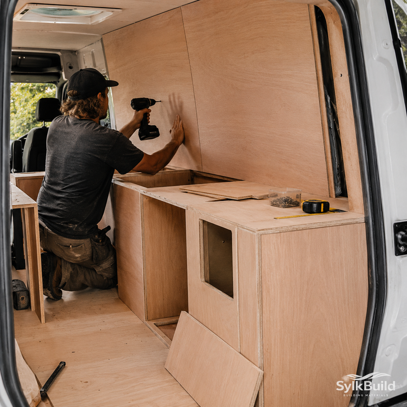 Person working on a wooden interior setup inside a van, using tools.